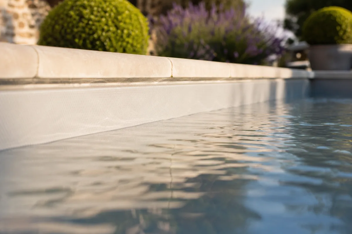 Bassin rénové avec membrane gris clair, eau limpide et margelles en pierre