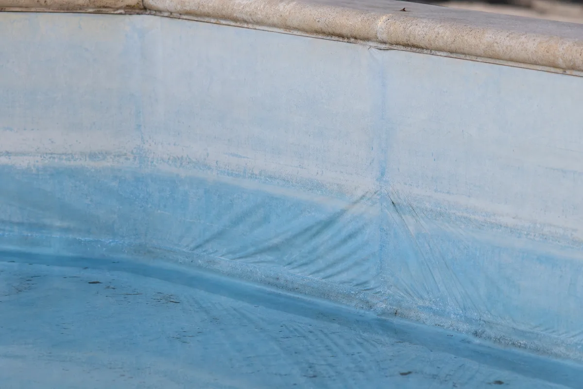 Liner de piscine décoloré sur la ligne d&rsquo;eau avec plis visibles dans un angle du bassin